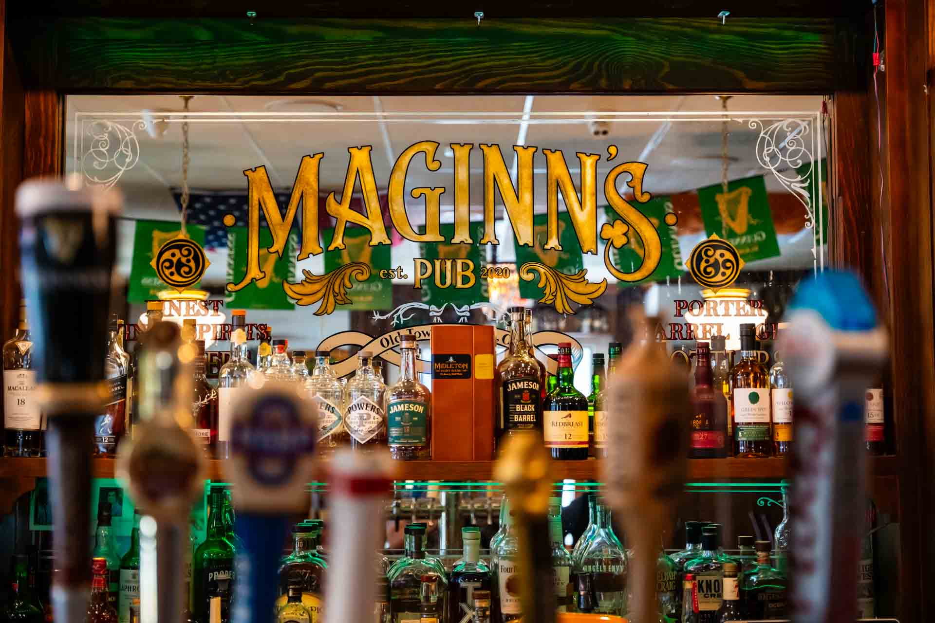 Interior of Maginn's Pub with a display of whiskey bottles and tap handles in front of a vintage-style sign