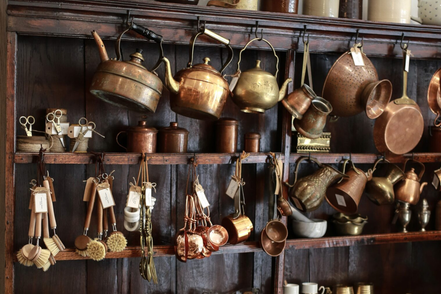 vintage stained cupboard adorned with brass tea kettles, brushes and other kitchen utensils