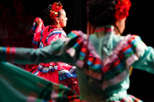 Dancers wearing colorful, layered dresses and floral headpieces perform traditional a Mexican Dance at the Newhall theatre